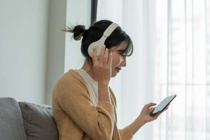 Femme pratiquant l'écoute musicale active avec casque et smartphone à la maison