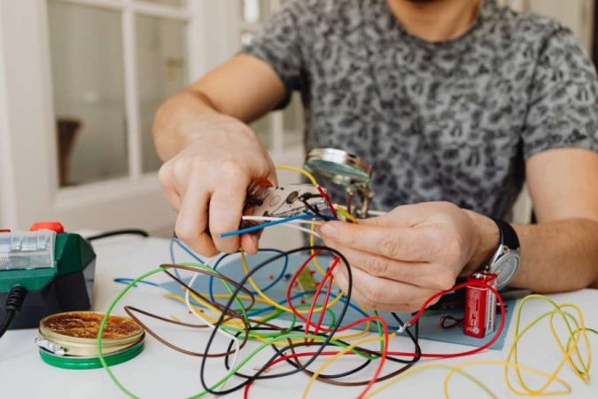 Homme manipulant une masse de câbles électriques colorés enchevêtrés sur une table, illustration du problème à résoudre pour cacher les câbles électriques.