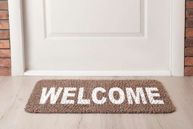 Un paillasson marron avec l'inscription "WELCOME" posé devant une porte blanche fermée pour une entrée accueillante.