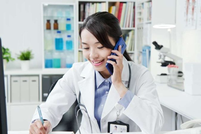 Un médecin de garde sourit en téléphonant tout en prenant des notes.