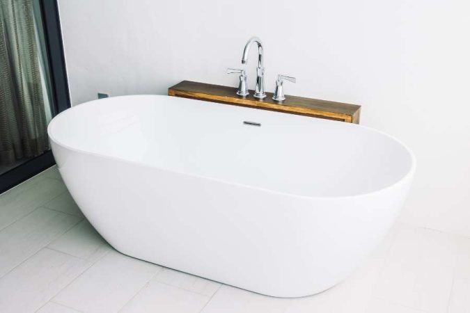 Baignoire îlot blanche au design moderne avec robinetterie chromée et tablette en bois.