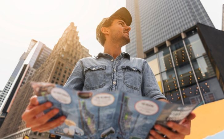 Jeune homme observant des immeubles en ville avec un plan pour investir locatif prix m2 rentabilité ciblée.
