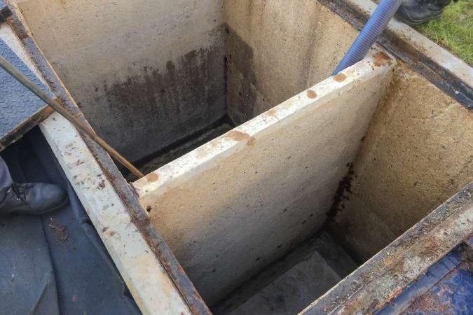 Vue en plongée d'un grand bac à graisse en béton ouvert lors de son nettoyage.